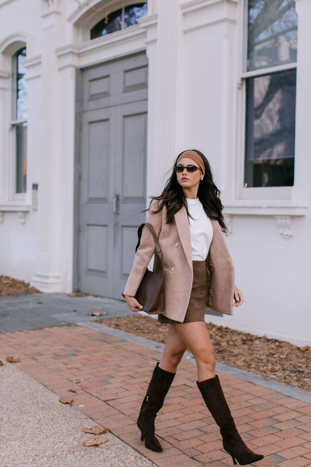 Woman in a stylish outfit walking on a sidewalk in front of a building.