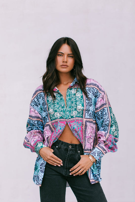 A woman wearing an oversized shirt with a paisley tile print in multiple colors including blue, pink, and green.