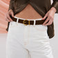 Person wearing a brown leather jacket and white jeans with a brown belt.