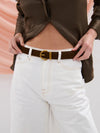 Person wearing a brown leather jacket and white jeans with a brown belt.