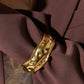 Gold statement cuff bracelet with intricate design worn on a dark brown blazer close up.