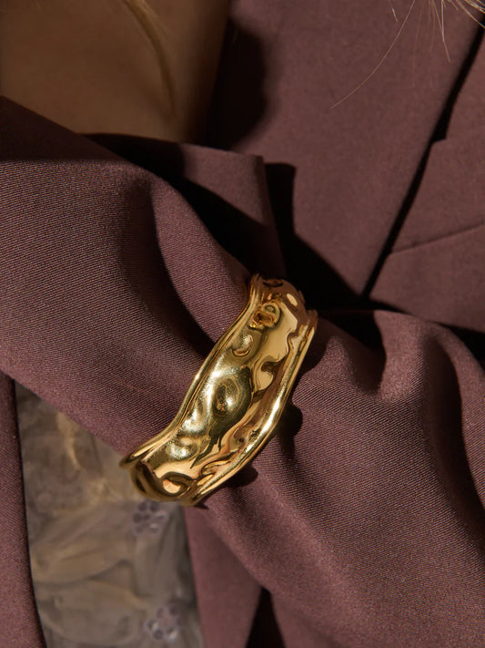 Gold statement cuff bracelet with intricate design worn on a dark brown blazer close up.