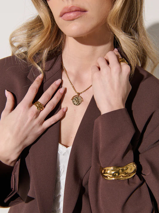 Woman wearing gold jewelry including a necklace, ring, and bracelet against a neutral background