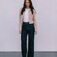 Woman wearing a beige jacket, white top, and dark jeans against a plain background
