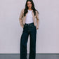Woman wearing a beige jacket, white shirt, and dark jeans against a plain background