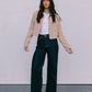 Woman wearing a beige jacket, white top, and dark jeans against a plain background
