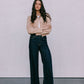 Woman wearing a beige jacket and dark jeans standing against a plain background