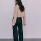 Woman wearing a beige jacket and dark jeans against a plain background