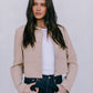Woman wearing a beige jacket over a white shirt and dark jeans on a plain background