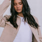 Woman wearing a beige blazer over a white top with a plain background