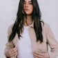 Woman wearing a beige jacket over a white shirt with a plain background