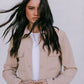 Woman wearing a beige jacket over a white shirt with long dark hair against a plain background