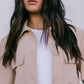 Woman wearing a beige jacket over a white shirt against a neutral background
