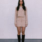 Woman wearing a beige outfit with black knee-high boots on a plain background