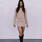 Woman wearing a beige outfit with black boots on a plain background