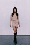 Woman wearing a beige outfit with black boots on a plain background