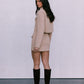 Woman wearing a beige suit and black knee-high boots against a white background