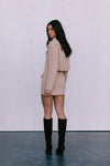Woman wearing a beige suit and black knee-high boots against a white background