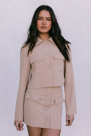 Woman wearing a beige two-piece suit against a white background
