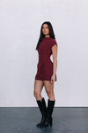 Woman wearing a burgundy dress and black knee-high boots against a white background