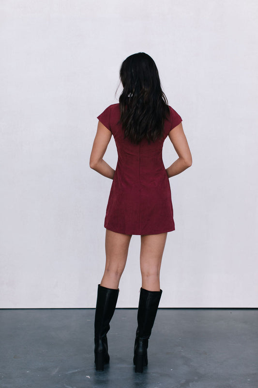Person wearing a red dress and black boots standing against a white wall.