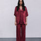 Woman wearing a burgundy outfit with a top and patterned pants on a plain background