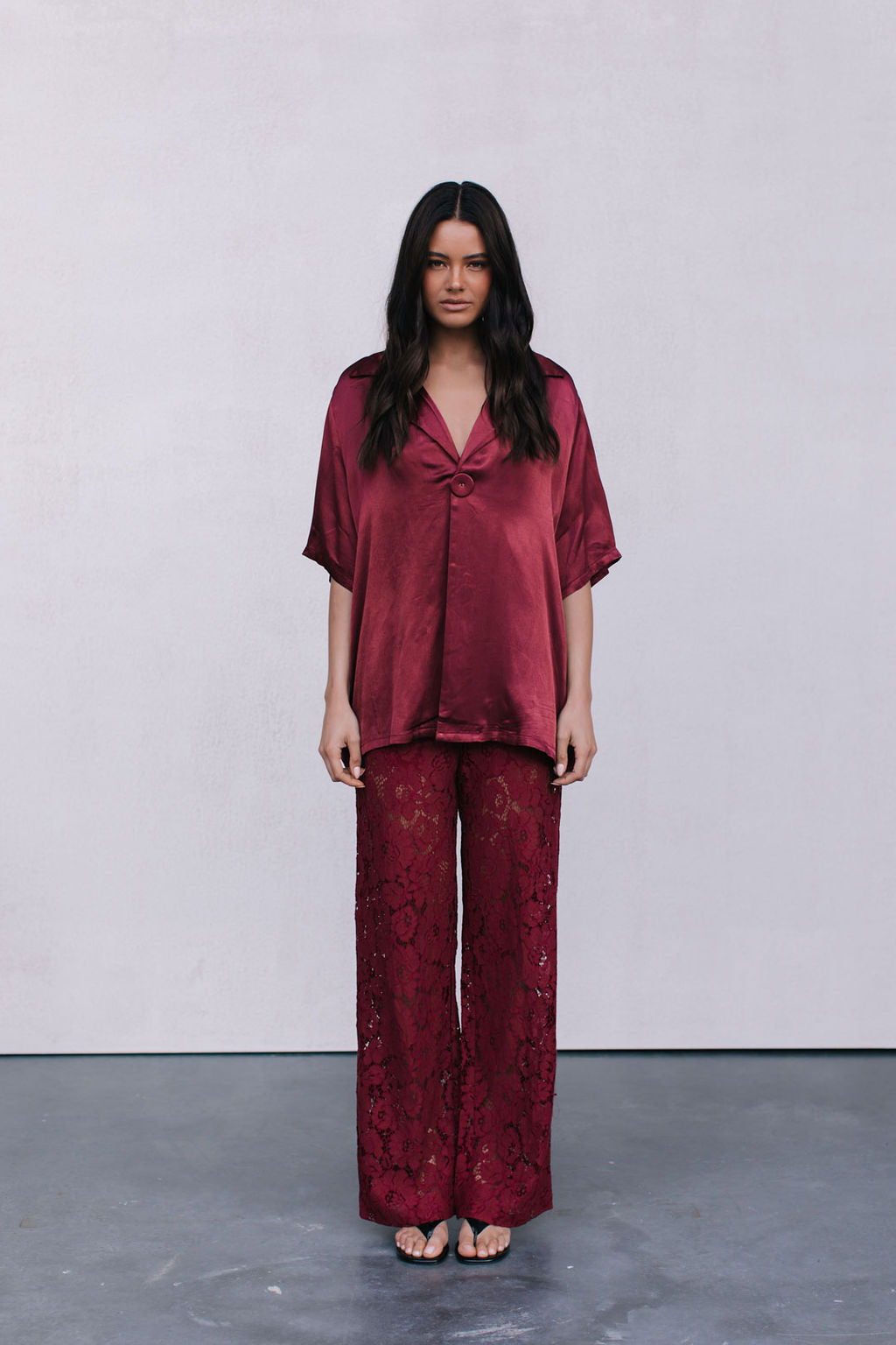 Woman wearing a burgundy outfit with a top and patterned pants on a plain background