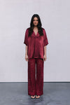 Woman wearing a burgundy outfit with a top and patterned pants on a plain background