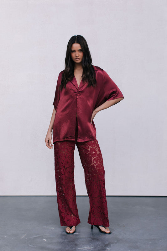 Woman wearing a burgundy satin outfit with lace pants on a plain background