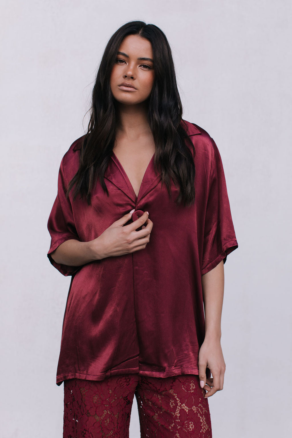 Woman wearing a burgundy satin shirt with lace pants on a white background