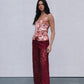 Woman wearing a floral top and burgundy pants against a plain background