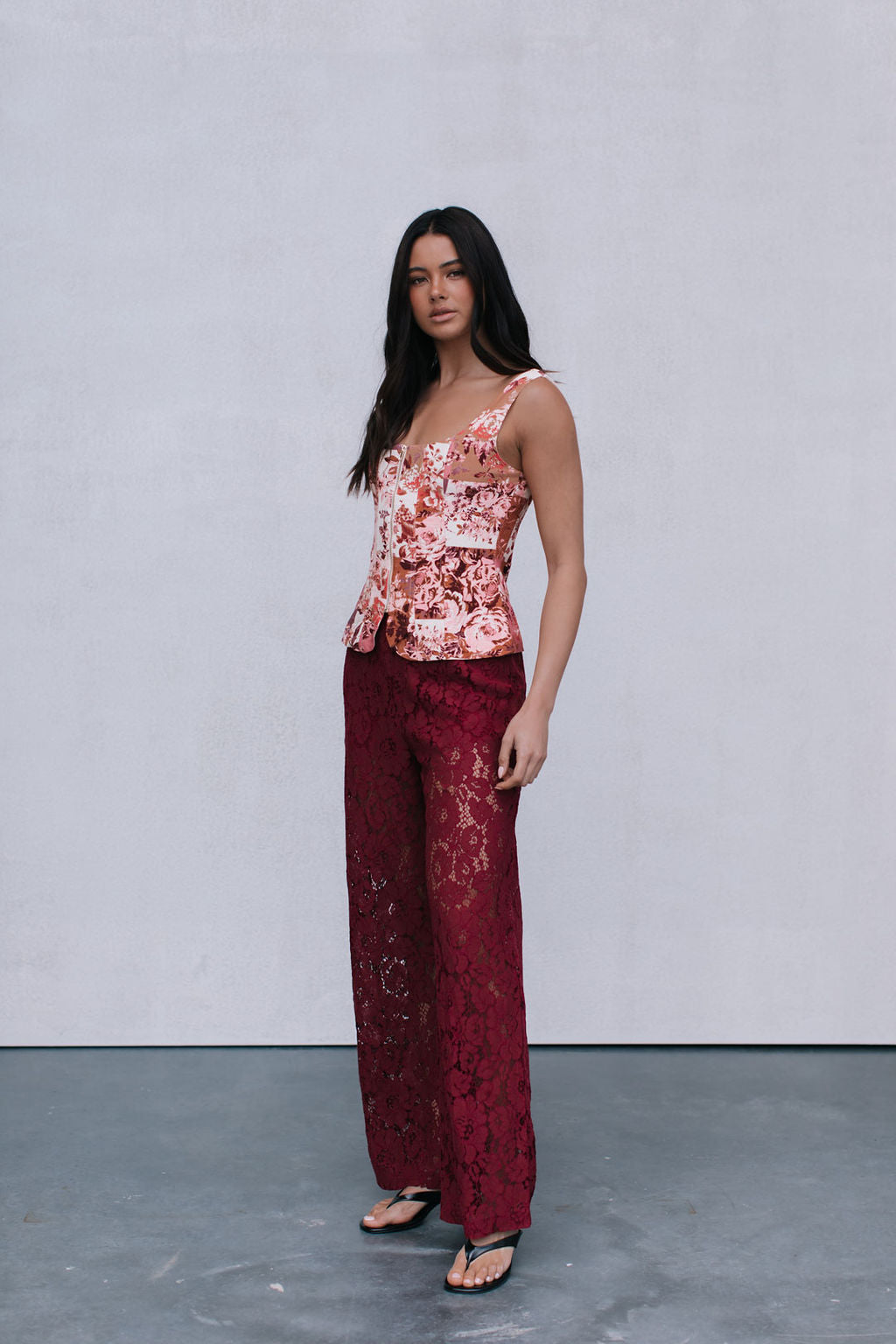 Woman wearing a floral top and burgundy pants against a plain background