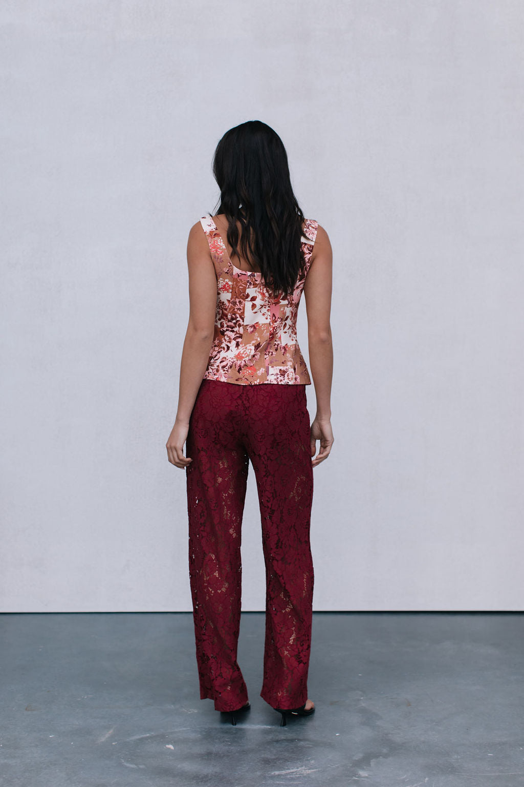 Woman wearing a floral top and red pants against a plain background