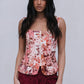 Woman wearing a floral top and burgundy pants against a plain background