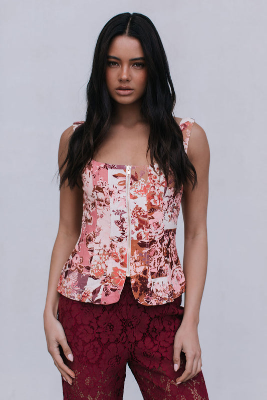 Woman wearing a floral top and burgundy pants against a plain background