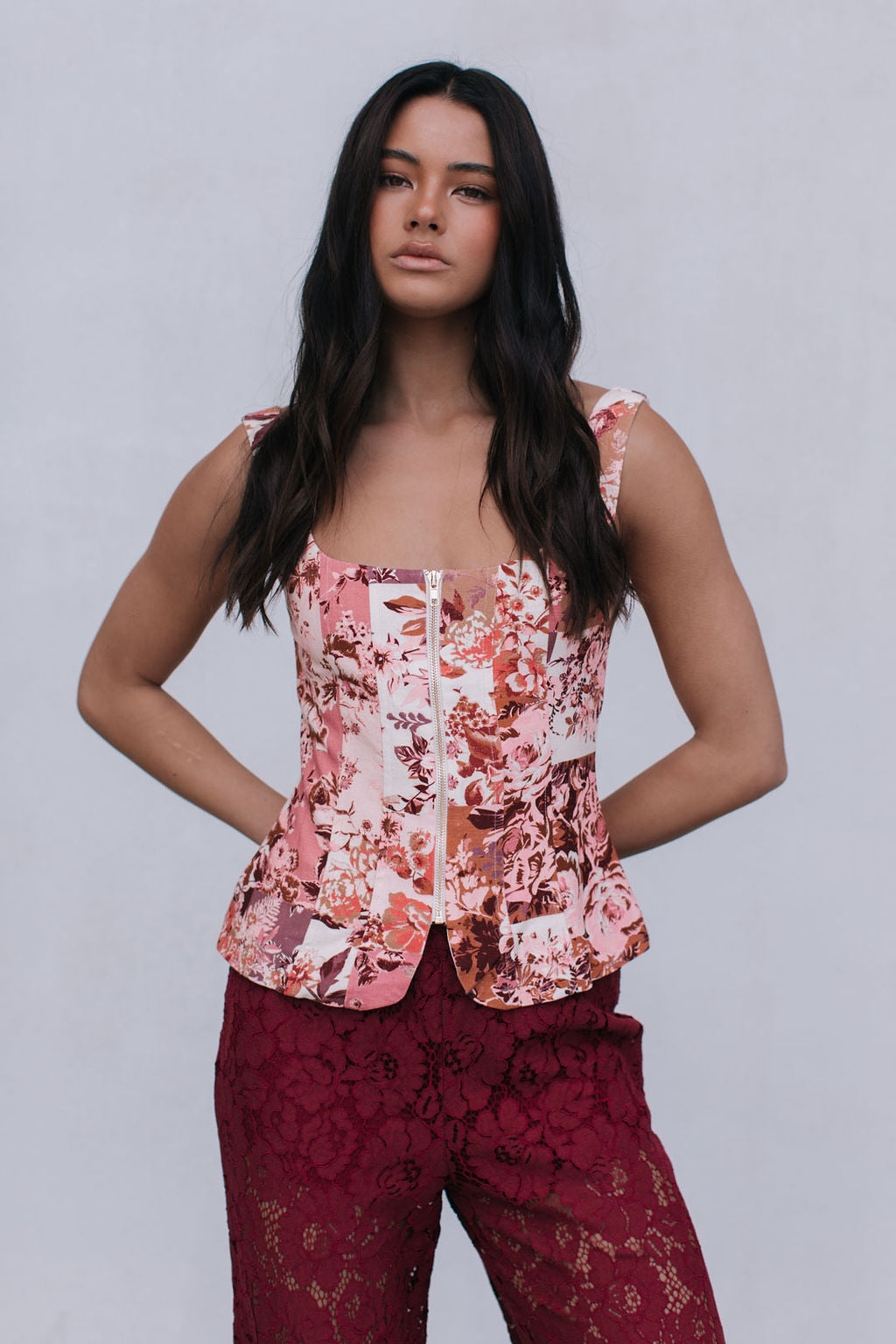 Woman wearing a floral top and burgundy pants against a plain background