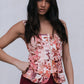 Woman wearing a floral top and maroon skirt against a plain background