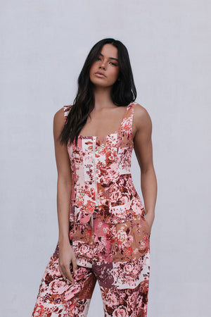 Woman wearing a floral jumpsuit pants and top against a plain background