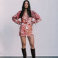 Woman wearing a floral skirt and blouse with puffed sleeves and brown knee-high boots against a white background