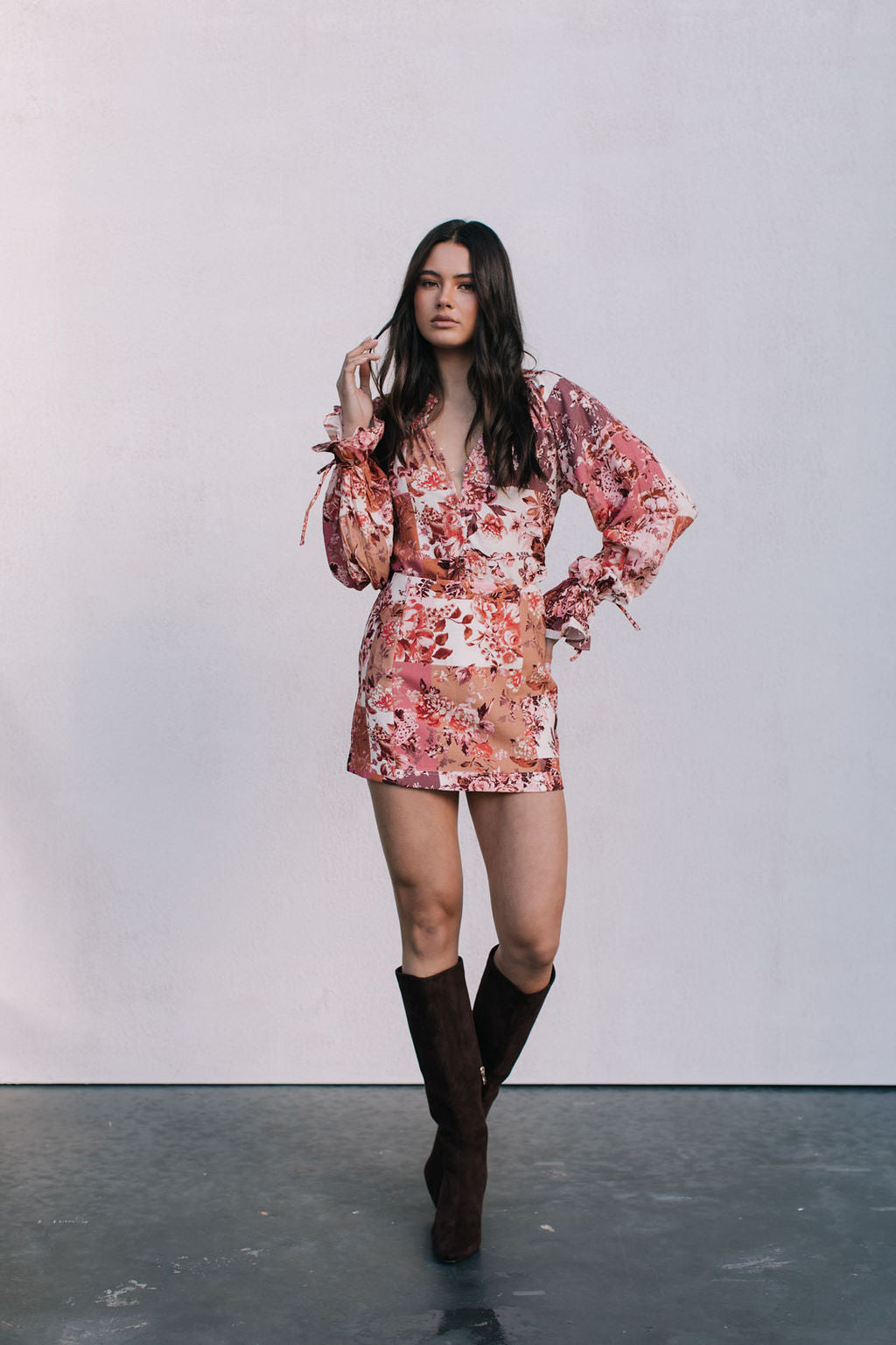 Woman wearing a floral dress and brown boots against a plain background