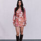 Woman wearing a floral dress with long sleeves and brown boots on a plain background