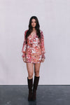 Woman wearing a floral dress with long sleeves and brown boots on a plain background