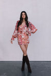 Woman wearing a floral dress with long sleeves and knee-high boots on a plain background