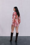 Woman wearing a floral dress and knee-high boots against a plain background