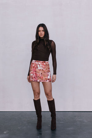 Woman wearing a brown top, floral skirt, and brown knee-high boots against a white background