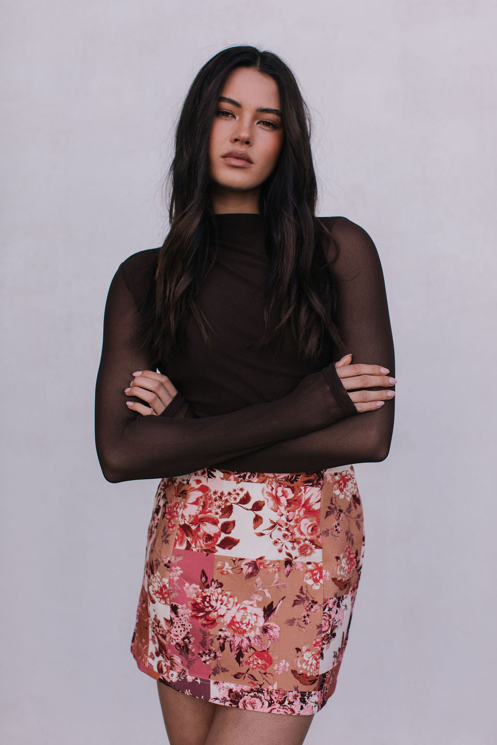 Woman wearing a floral skirt and black top against a plain background