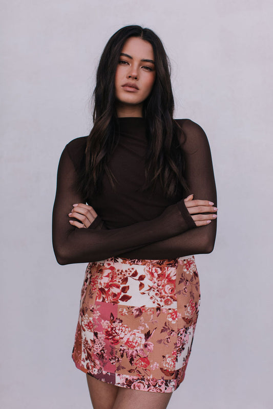 Woman wearing a floral skirt and black top against a plain background