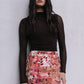 Woman wearing a brown top and floral skirt against a plain background