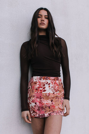 Woman wearing a brown top and floral skirt against a plain background