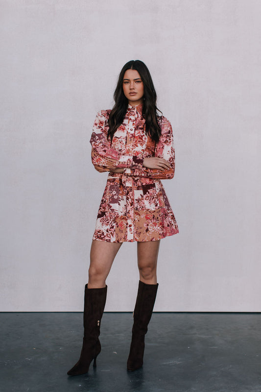 Woman wearing a floral dress and knee-high boots against a plain background